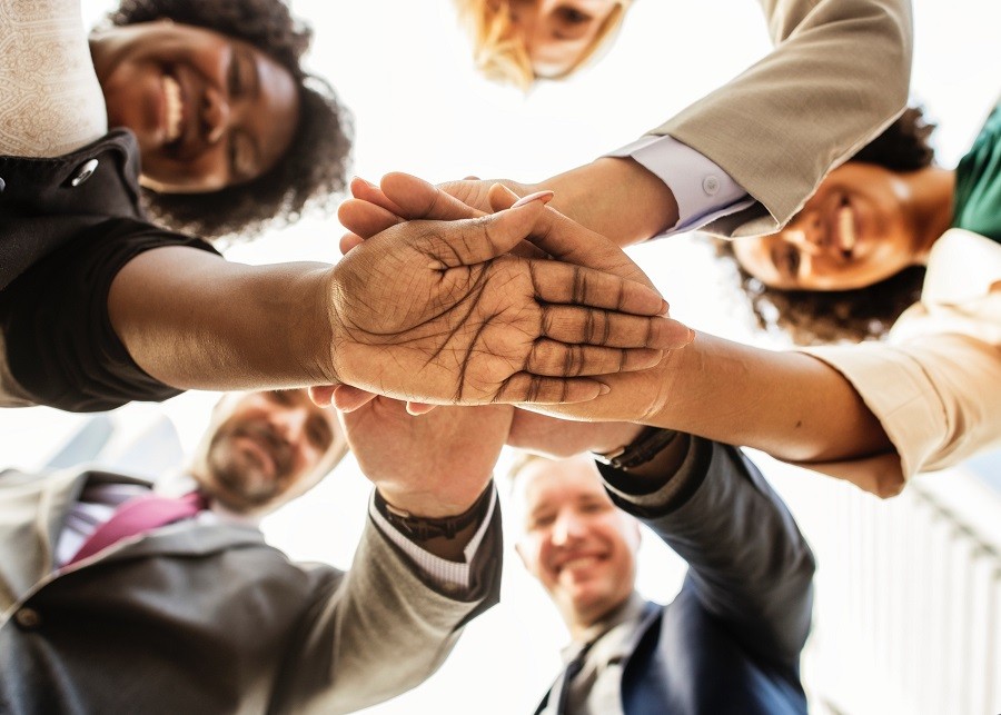 group of five smiling adults in a huddle with their hands stacked on top of each other.