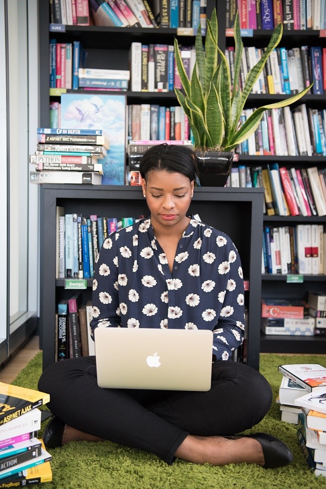 Female sitting on floor with laptop surrounded by books and bookshelves in the background