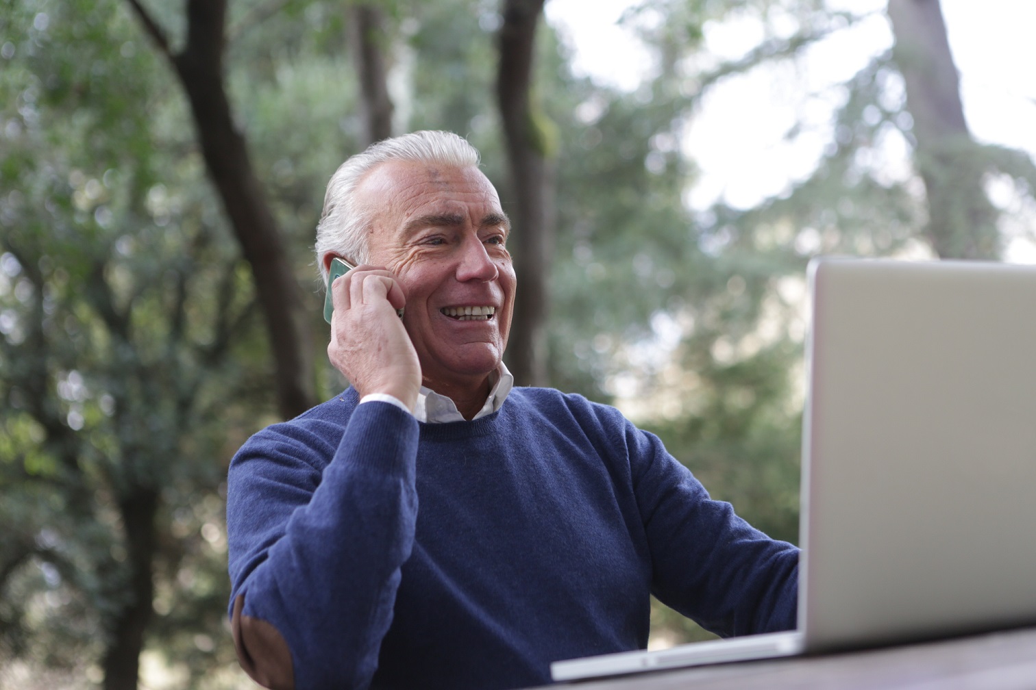 older maile talking on phone with laptop in front of him 