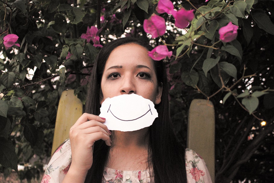 sad woman covering her mouth with a drawing of a smile