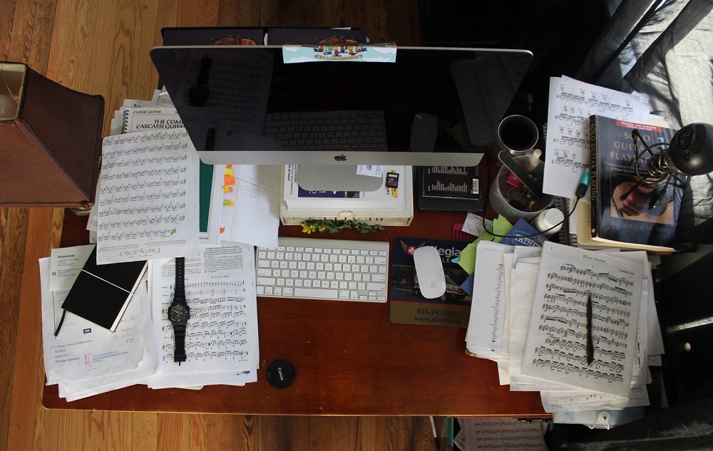 view of a desk from above with computer monitor and stacks of papers
