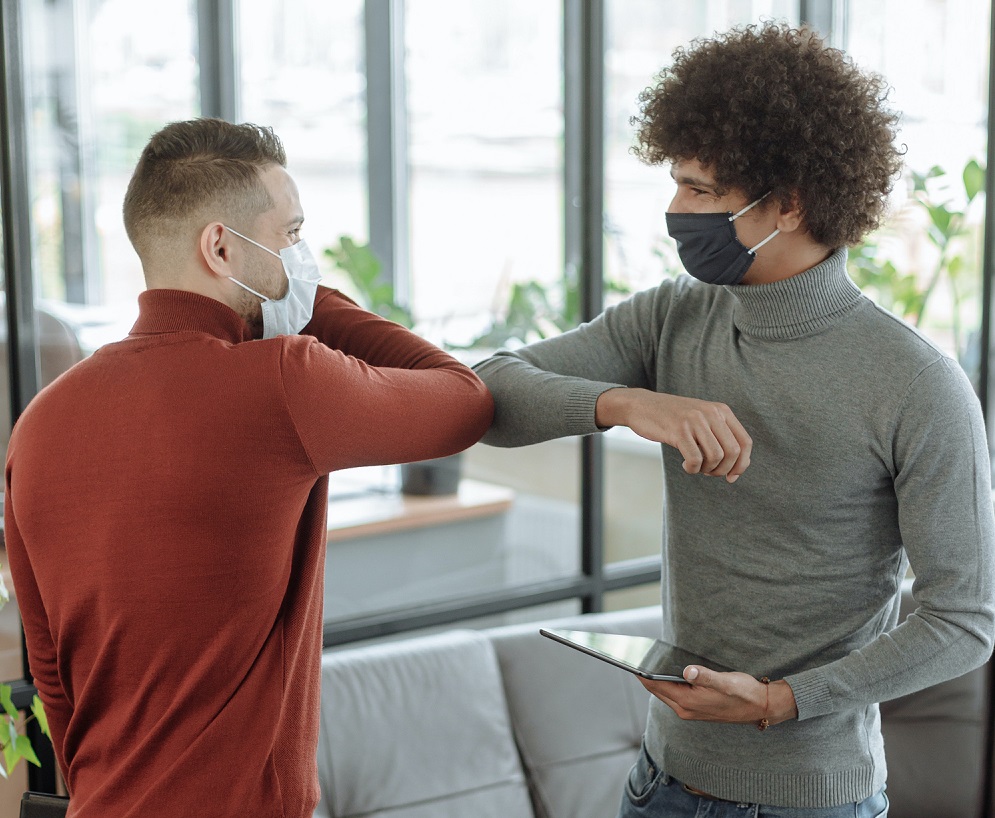 two men wearing masks elbow bumping