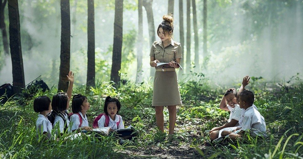 seven elementary students sitting outdoors with teacher standing 