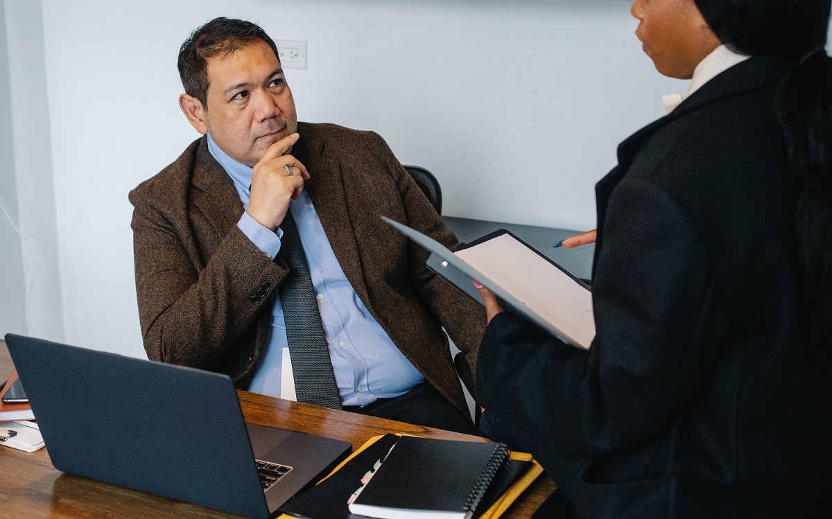 man sitting at desk in front of laptop looking annoyed at a female colleague 