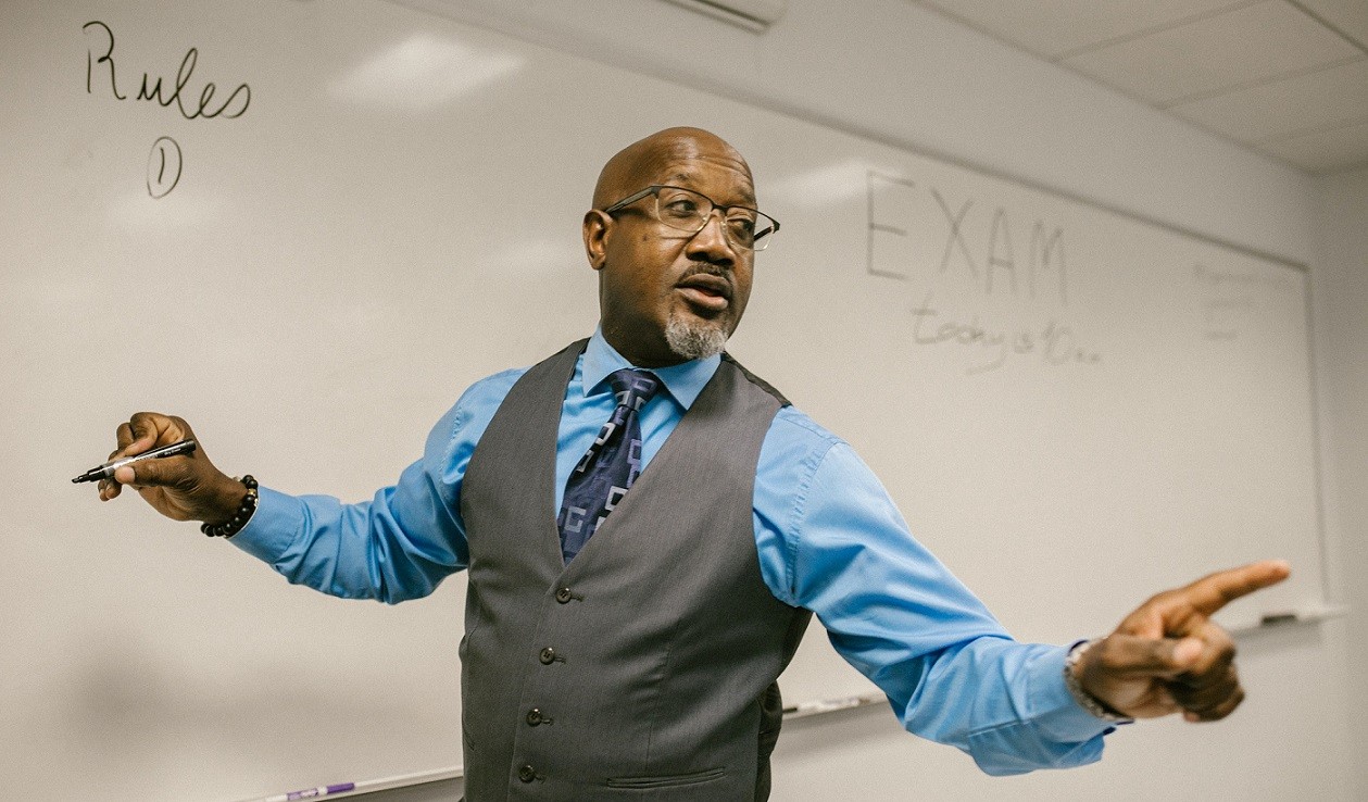 male teacher writing on white board and pointing with his other hand