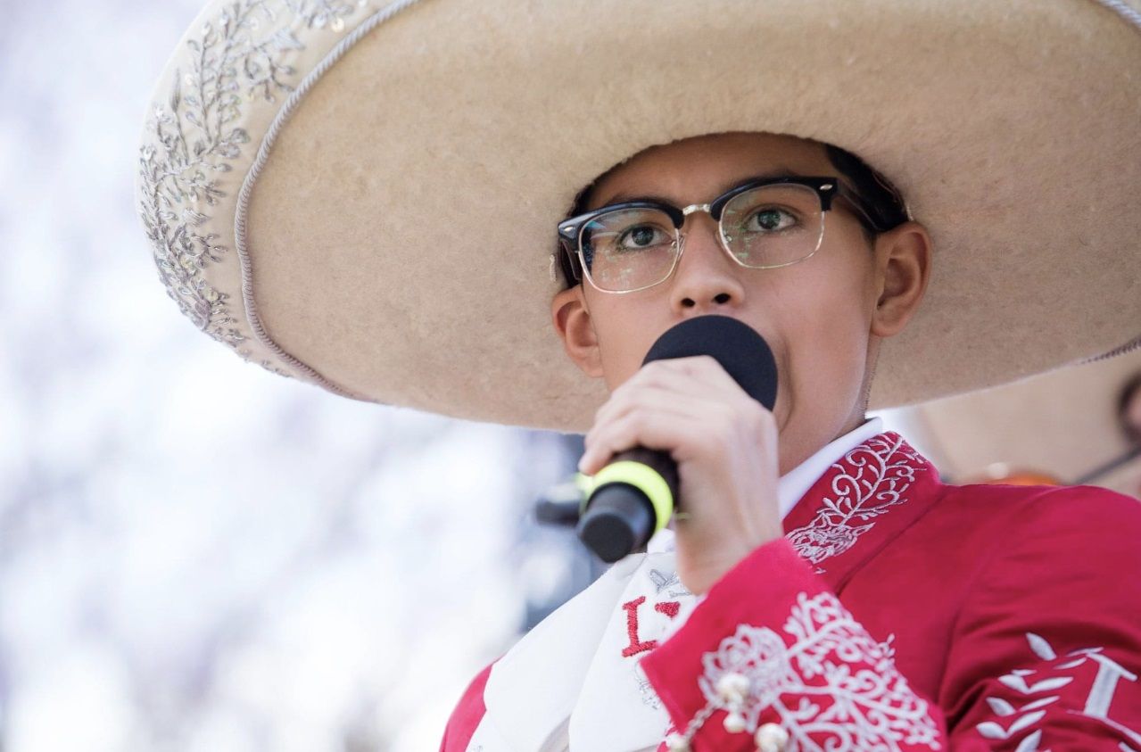 mariachi ensemble on stage holding sombreros over their heads 