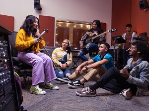 A group of band students listening to one of the band members in the rehearsal room.