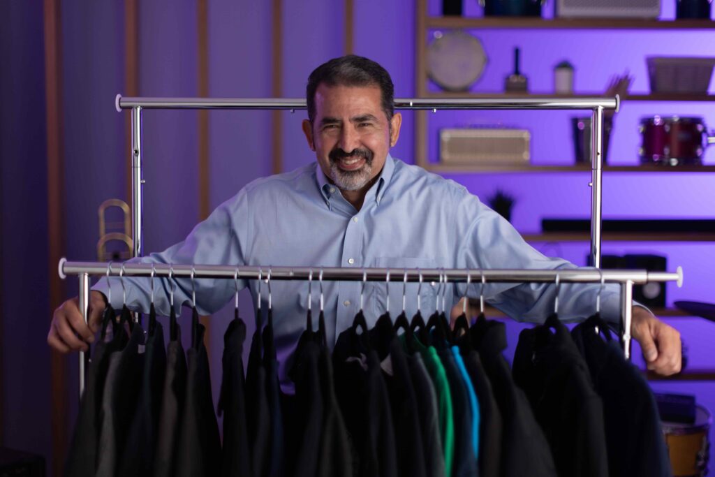 A smiling man in front of a wardrobe bar with jackets hanging.