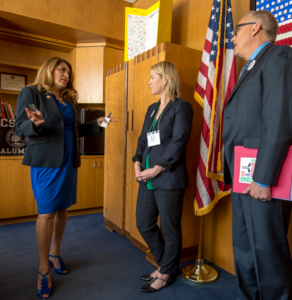 Two women and a man in front of a flag.