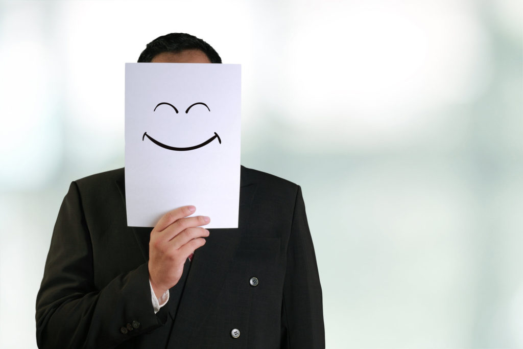 Man holding a drawing of a smiley face in front of his face.