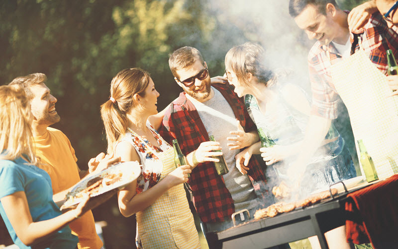 BBQ backyard Group of men and women laughing and holding plates of food next to a grill in a backyard.