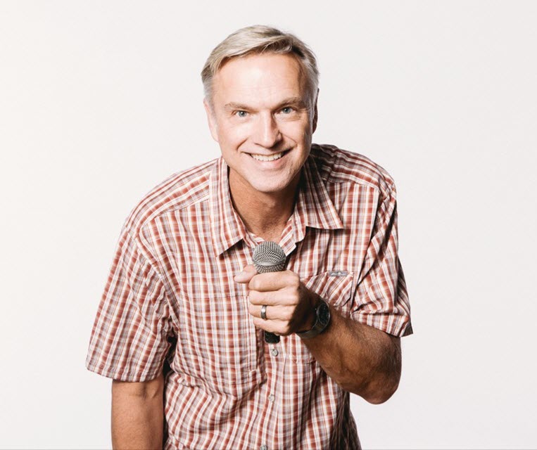 Man smiling and holding a microphone facing the camera.