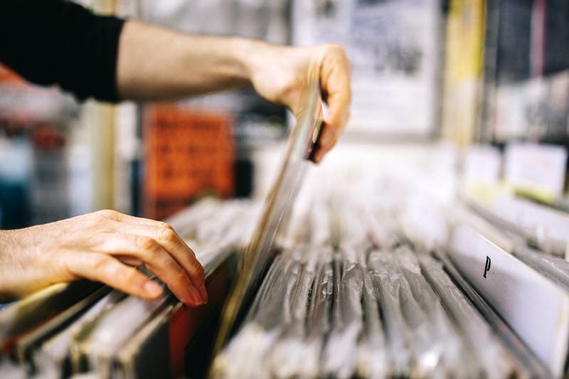 A man's hands as he selects a particular album out of a record store bin of albums.