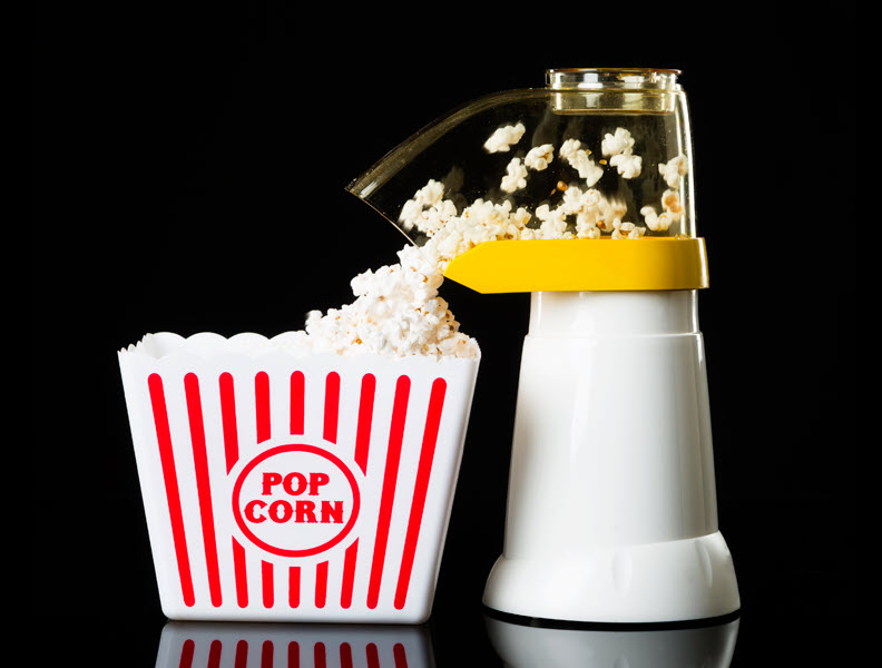 Air popper popping popcorn and it falling into a serving container.