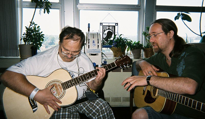Two men seated with acoustic guitars.