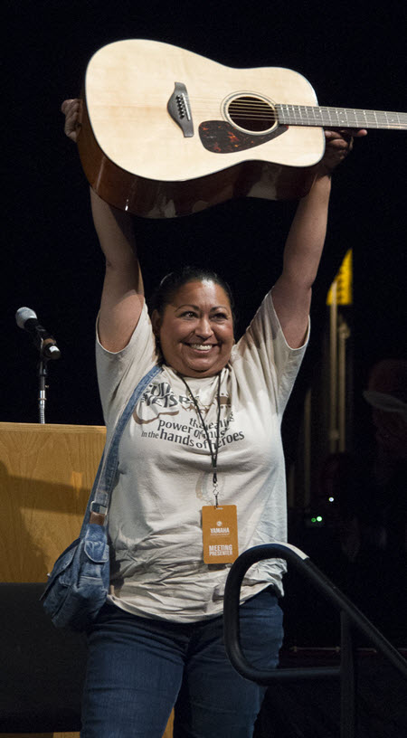 Young smiling woman holding an acoustic guitar over her head.