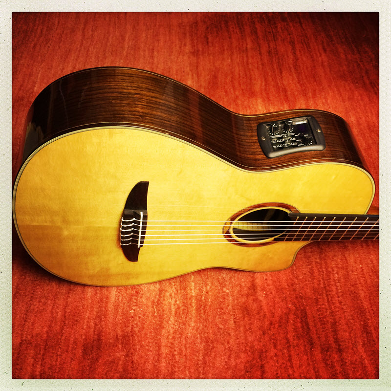 HipstamaticPhoto-555205327.113460 800wide Acoustic guitar laying on its side on a wood surface.