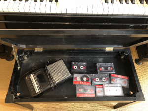 Interior of a piano bench showing a portable cassette player and cassettes.