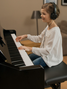 Young girl playing piano while wearing headphones.