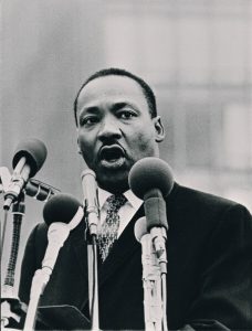 Dr. Martin Luther King watermarked Dr. Martin Luther King speaking behind four news microphones.