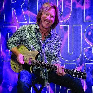 The author is sitting while holding a guitar.