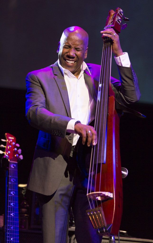 Man in a suit smiling while he plays an electric upright bass (EUB).