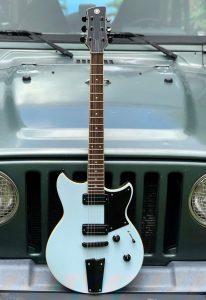 Electric guitar standing on a bumper of a jeep.