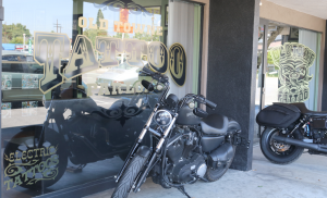Viewed from outside, the front windows of the Old Towne Tattoo Parlor with two Harley Davidson motorcycles parked on the sidewalk directly in front.