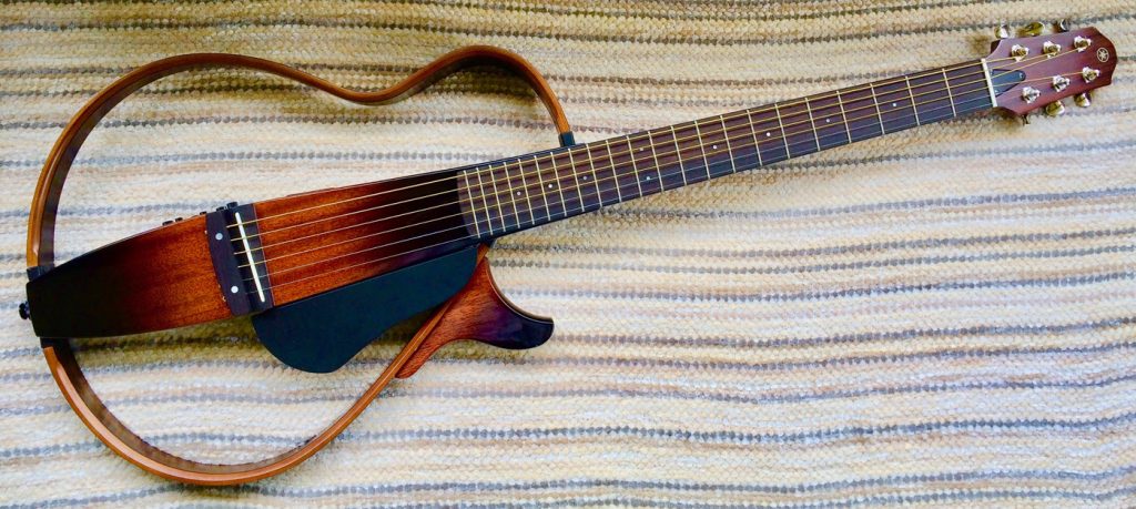 An acoustic guitar with an entirely open body laid on a striped woven cloth.