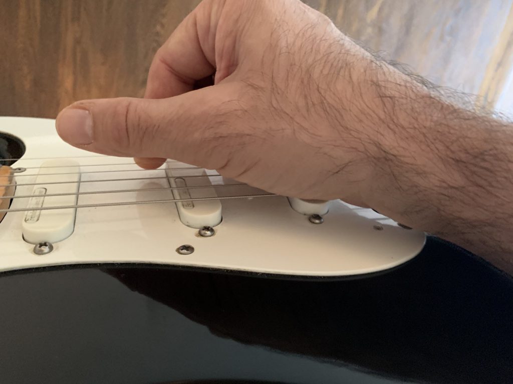 playslidept2fig.-4 Closeup of a man's hand plucking a string on an electric guitar.