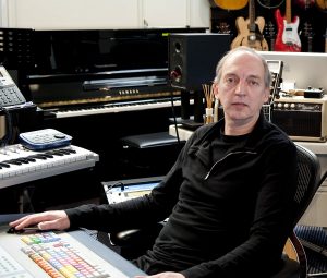 Stephen-Lipson-in-Studio_crop Middle aged man behind a sound board and surrounded with studio equipment.