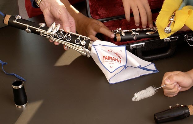 Closeup of table top with pieces of various woodwind instruments and several people cleaning them.