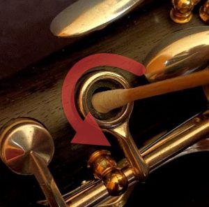 Graphic of a cotton swab in a woodwind tone hole with arrow showing movement in a circular direction.
