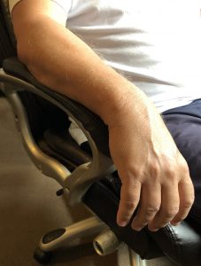Warm-up-Image-5a_Hand-at-Rest Closeup of a man's arm resting on the armrest of a rolling desk chair.