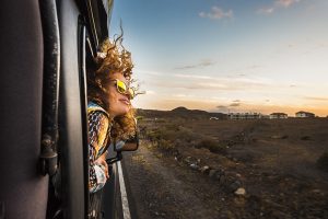 Young woman travels outside a railroad car with wind in the curly hair, motion and movement on the road discovering new places during a nice sunset.