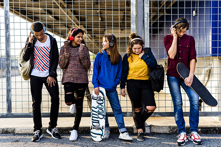 Group of school friends outdoors listening to music on ear buds and headphones.