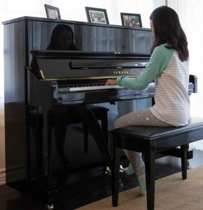 U series Young girl plays upright piano in living room.