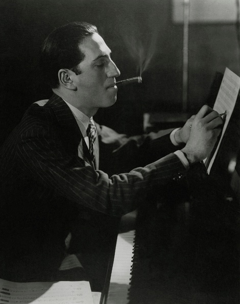 GettyImages-507042878 American composer George Gershwin sitting at a piano, smoking a cigar and writing on sheet music.