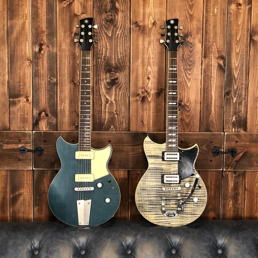 Sibling Harmony body_feature image Two electric guitars resting on leather couch with wooden backdrop.