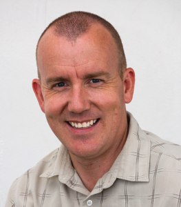 Russ-H-headshot-High-res Caucasion man approximately 40 years old smiling into the camera. You see him from the shoulders on up,.