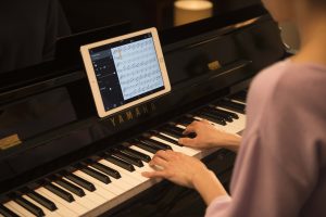 Woman playing Yamaha piano with iPad on music stand.