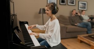 A smiling little girl playing a SILENT piano while wearing headphones.