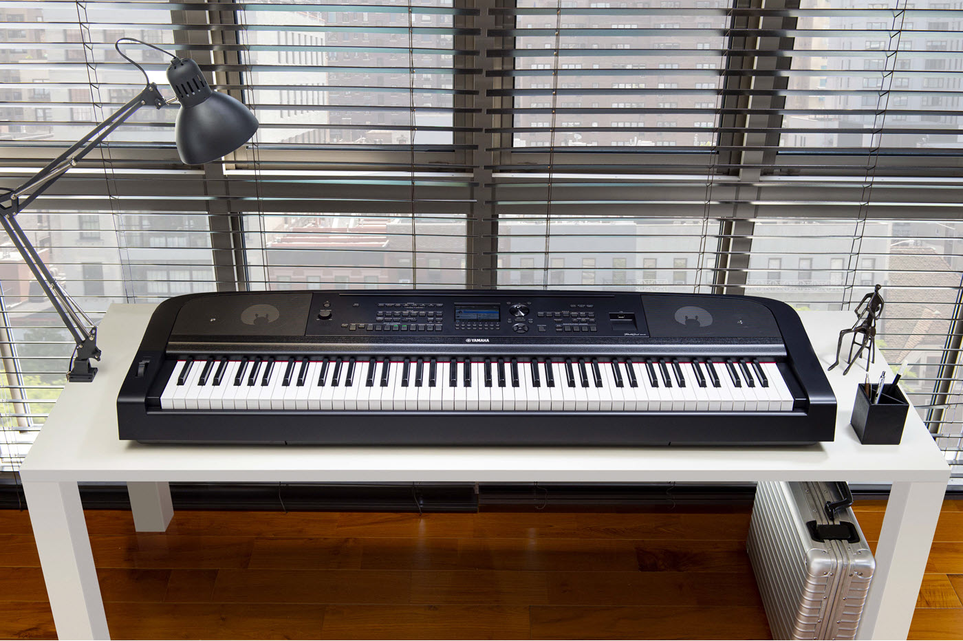 Digital piano keyboard on a desk in front of a window in a highrise apartment.