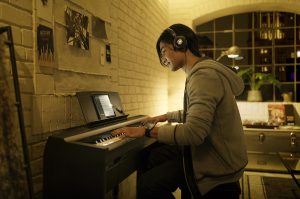 Boy playing a digital piano while wearing headphones.