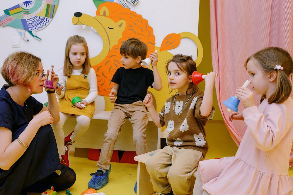 female teacher with group pf elementary students holding hand bells