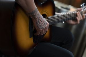 Closeup of Keith Urban's tattooed arm and hand holding the guitar by the neck.