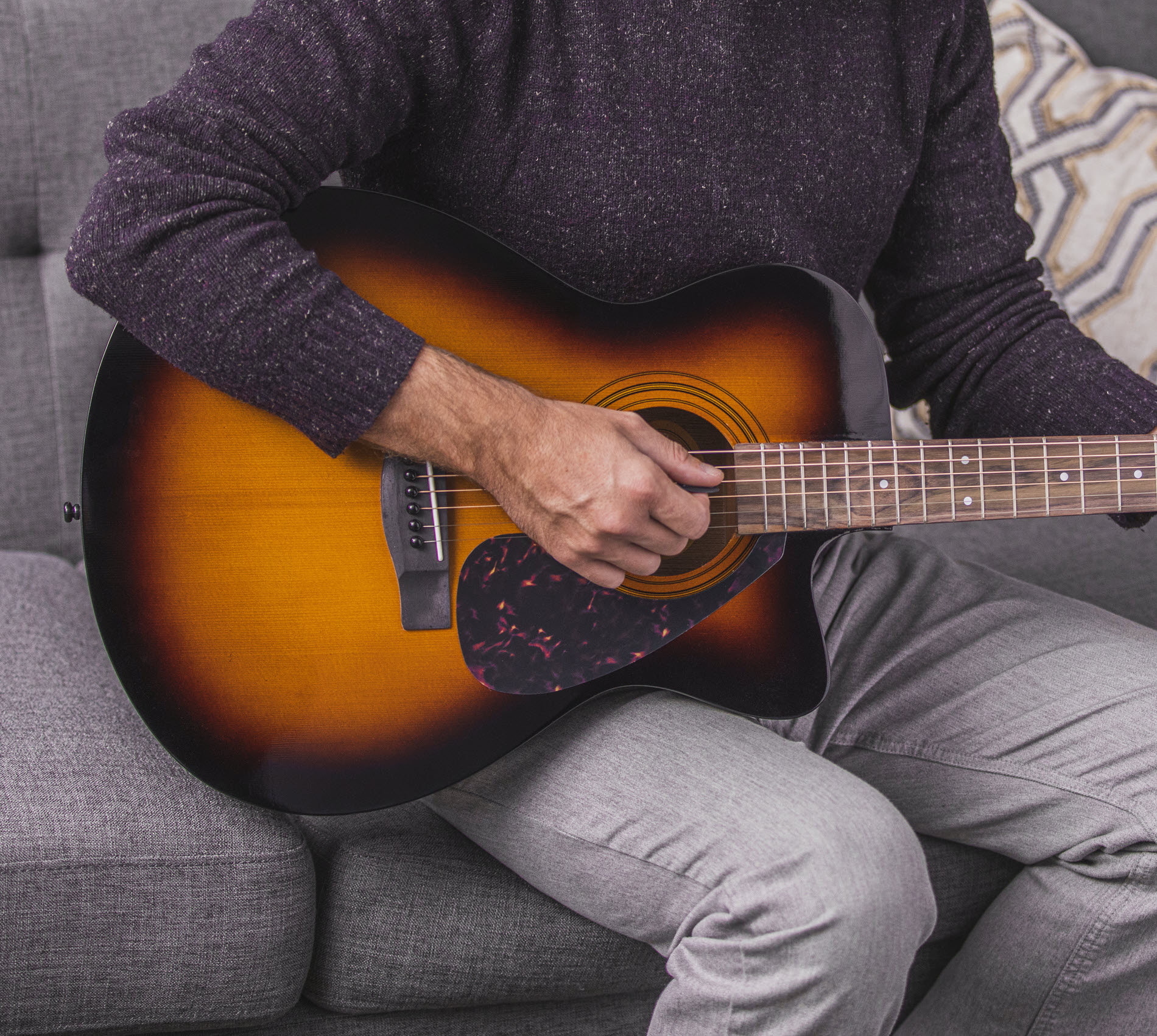 guitar-tips1 Closeup of someone seated on a couch playing an acoustic guitar.