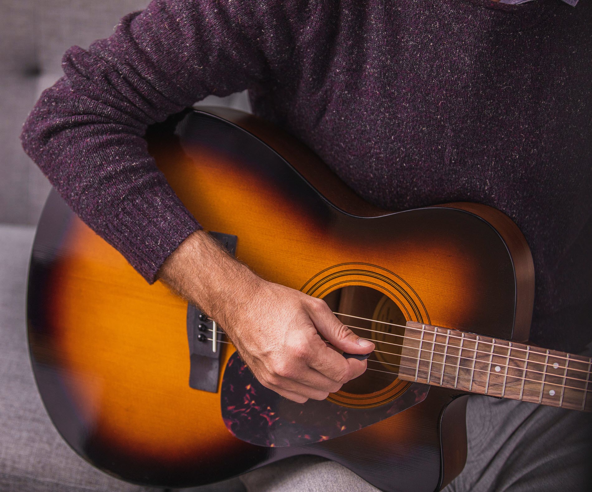 guitartips3 Closeup of someone seated on a couch playing an acoustic guitar.