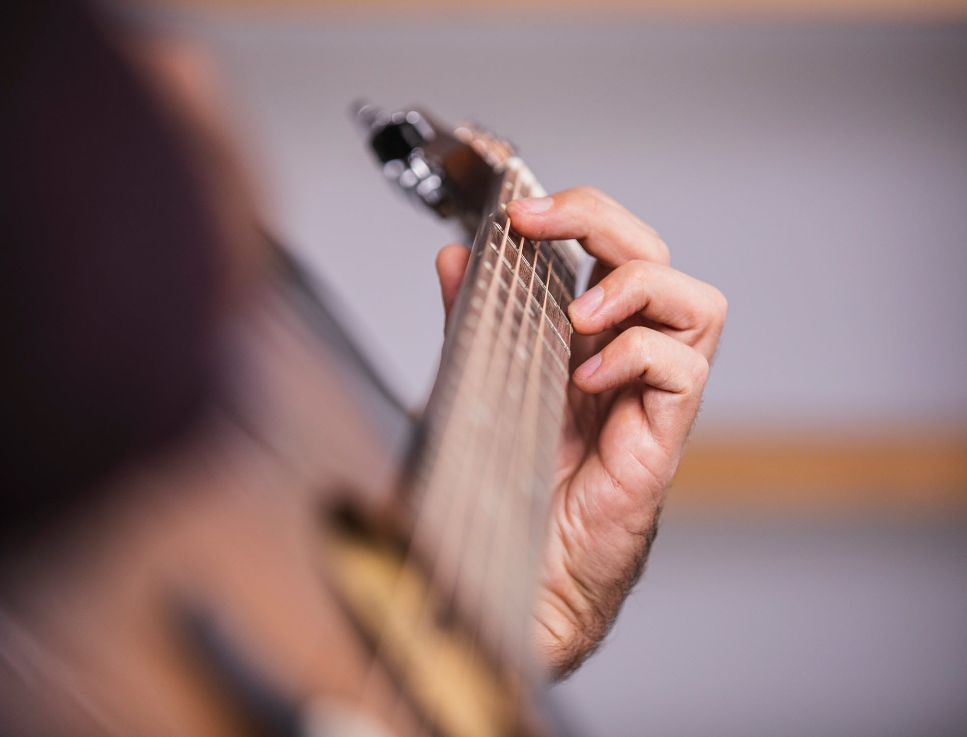 guitartips4 Closeup from side angle of someone playing an acoustic guitar with focus on hand placement on neck of guitar.