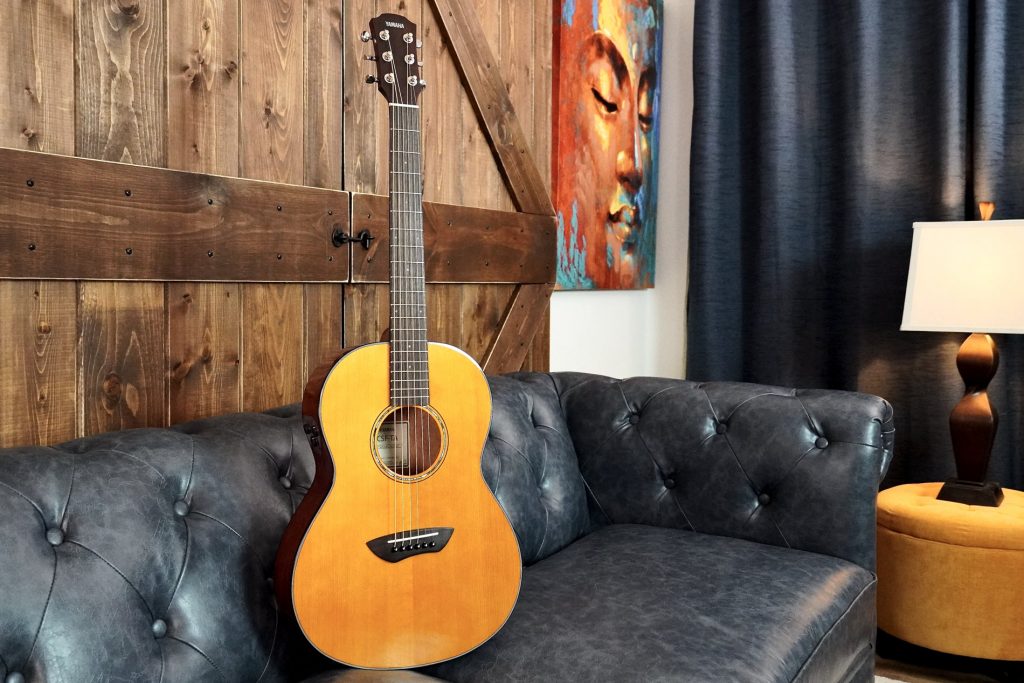 CSFTA Acoustic guitar propped on leather couch in masculine living room.